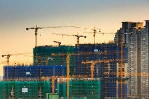 A silhouetted construction crane with a sunset backdrop from the city represents an article about the Benefits of Getting a Business Loan for Construction Companies.