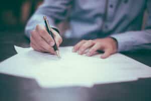 A man signing a document with a pen while following the steps to getting a small business loan.