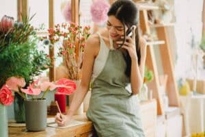 A woman in a floristry is on the phone asking questions about small business loans vs. personal loans that will help her choose the right one.