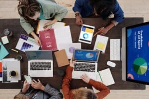 A group of professionals gathered around a table, focused on their laptops and surrounded by papers, discussing the Differentiation Business Strategy.