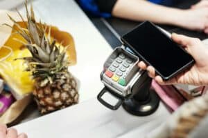 A person in a coffee shop holding a smartphone to process a tap payment represents how businesses can benefit from cash flow business loans.