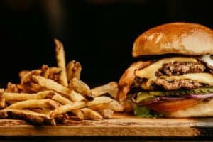 An image of a delicious hamburger and crispy french fries on a wooden cutting board represents an article about restaurant cash advance loans for small businesses.