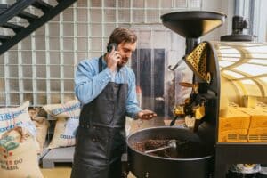 A coffee factory owner compares loan rates for small businesses with a loan officer on a phone call.