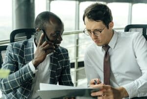 Two businessmen in suits are sitting at a table, discussing how merchant cash advance loans can help them in their business.