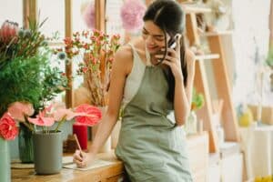 A picture of a female small business owner in a flower shop, answering a phone call to take an order, represents an article about small business loan requirements.