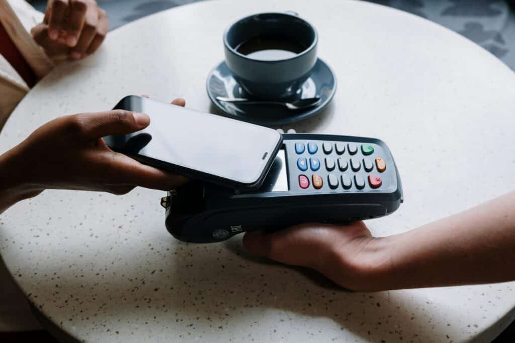 An image of a person with a phone tapping to pay at a restaurant represents the financial aspects of a business line of credit and it’s costs.