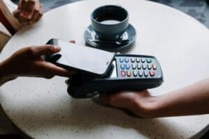 An image of a person with a phone tapping to pay at a restaurant represents the financial aspects of a business line of credit and it’s costs.