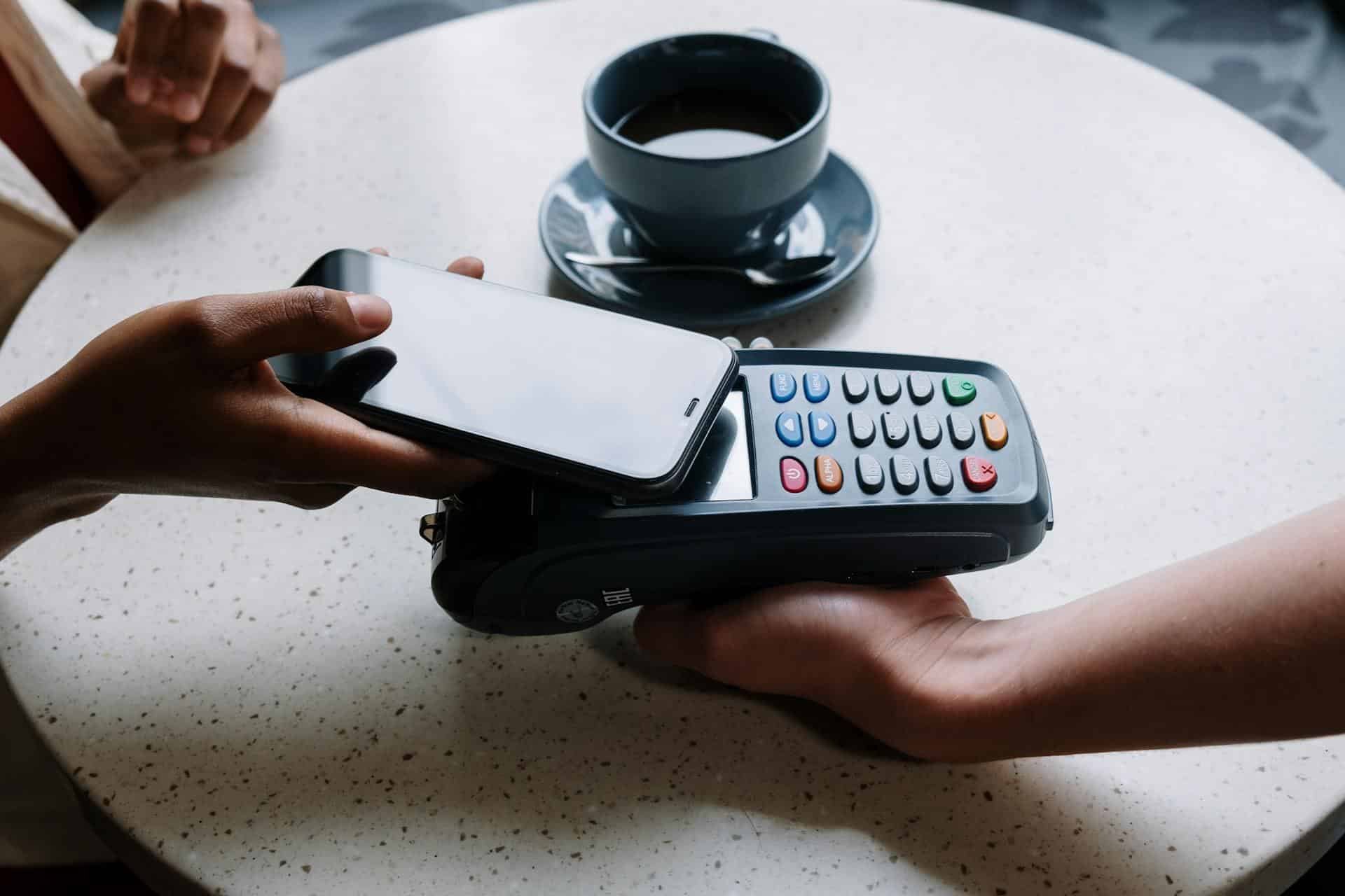 An image of a person with a phone tapping to pay at a restaurant represents the financial aspects of a business line of credit and it’s costs.